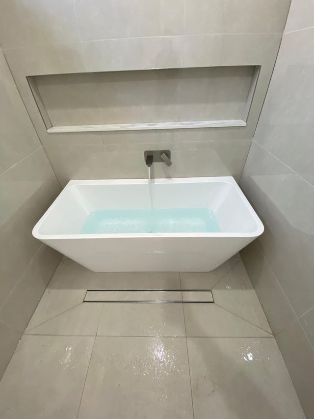 Wall-mounted bath mixer and spout running cleanly into a freestanding bath after fit-off
