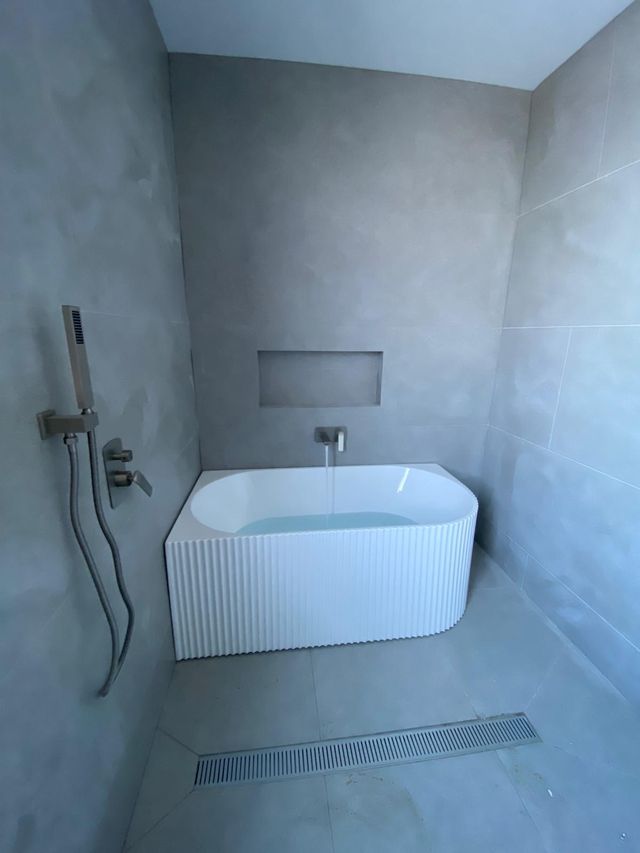 Fluted freestanding bath and wall mixer in a microcement-finished bathroom with a linear floor waste