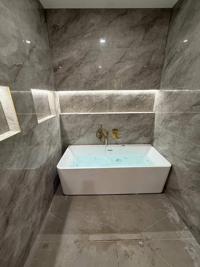 Freestanding bath with brushed gold tapware in a completed marble-tiled Melbourne bathroom