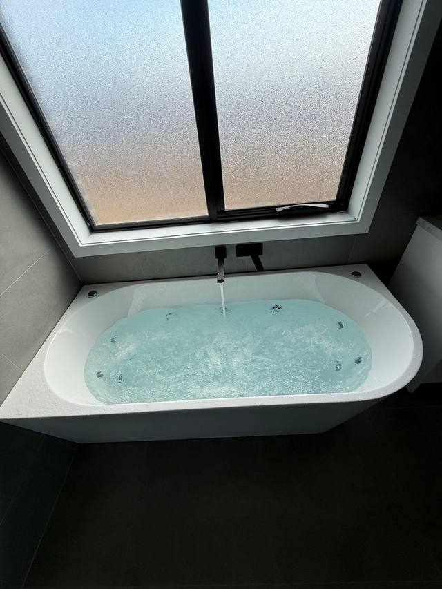 A spa bath filling with hot water in a finished Melbourne bathroom