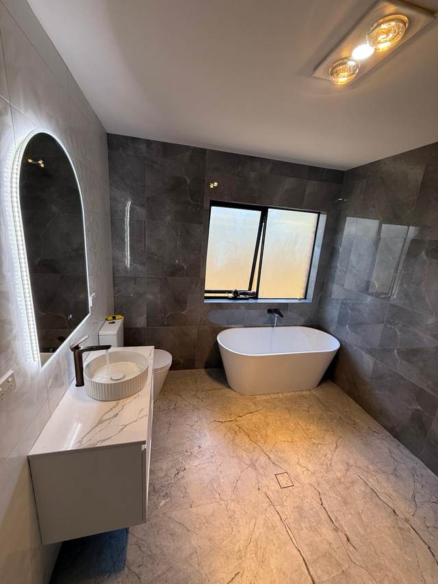 Completed bathroom renovation with a freestanding bath, wall-hung vanity and dark stone tiling