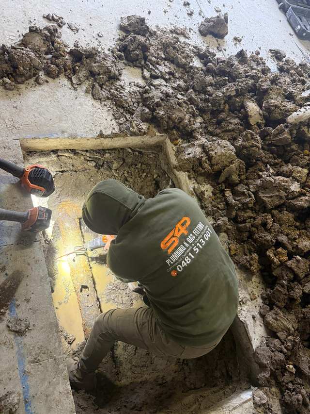 An S4P plumber working in an excavation cut through a concrete slab to reach a blocked drain line