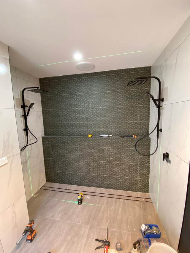 Twin rail showers being fitted off against a patterned feature tile wall with a linear floor waste