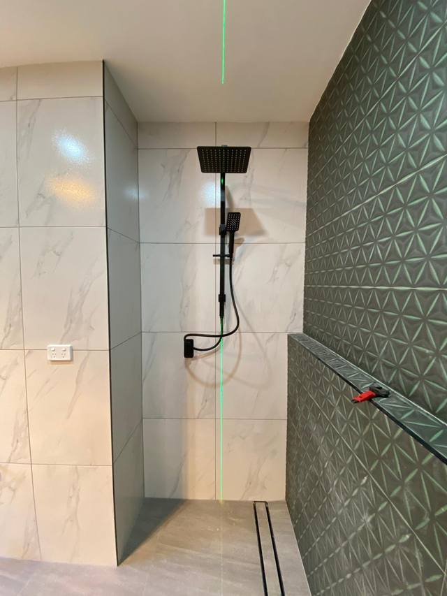 Black rail shower and mixer fitted against marble-look tiling beside a green feature wall